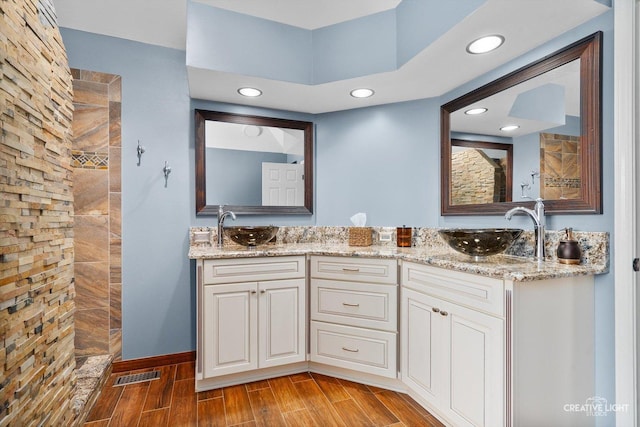 full bath featuring wood finish floors, a tile shower, recessed lighting, double vanity, and baseboards