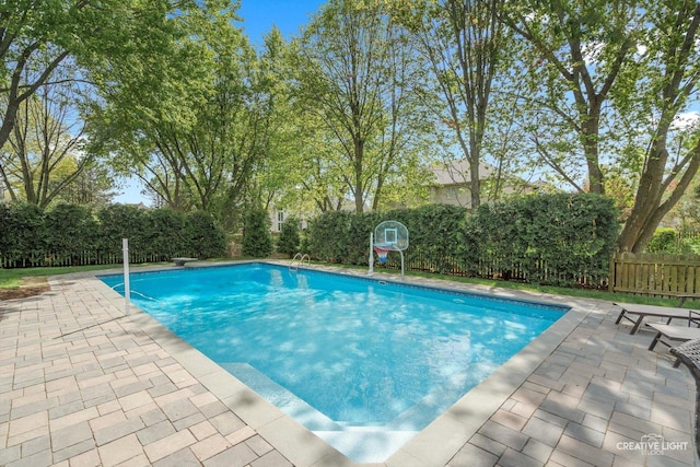 view of pool featuring a patio area, a fenced backyard, and view of scattered trees
