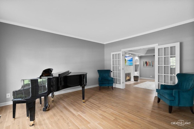 sitting room featuring french doors, crown molding, baseboards, and light wood-style floors