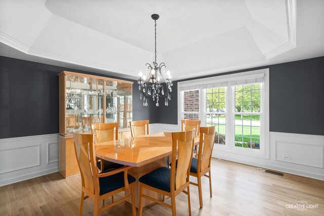 dining space with a raised ceiling, wainscoting, light wood-type flooring, a chandelier, and a decorative wall