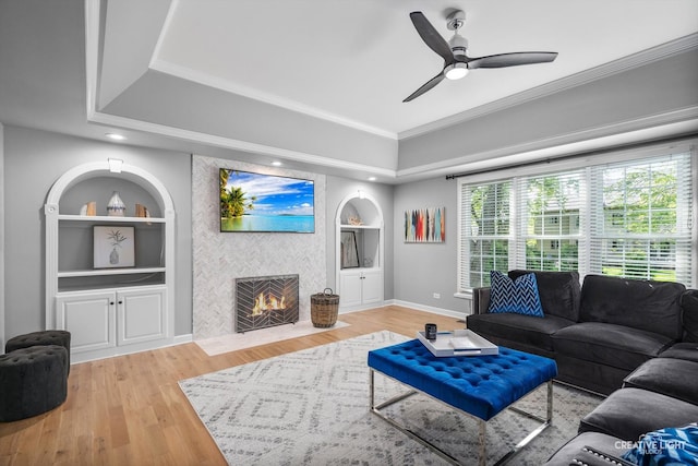 living area featuring built in shelves, a tile fireplace, ceiling fan, wood finished floors, and ornamental molding