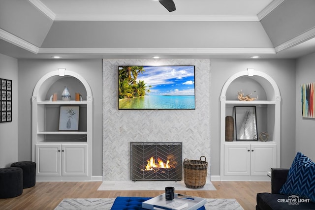 living room featuring built in shelves, vaulted ceiling, crown molding, wood finished floors, and an accent wall