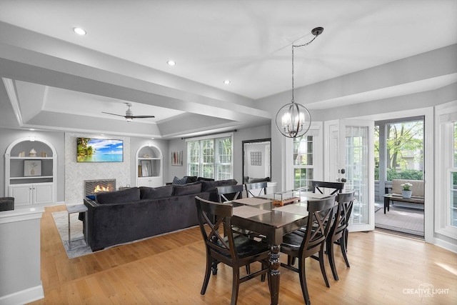 dining room featuring a raised ceiling, built in features, light wood finished floors, a lit fireplace, and a chandelier