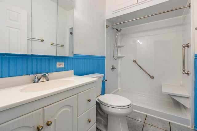 bathroom featuring tile patterned flooring, toilet, vanity, wainscoting, and walk in shower