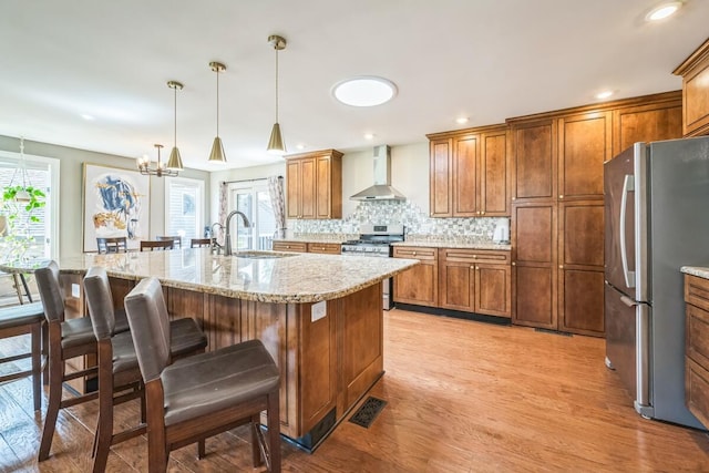 kitchen featuring light wood finished floors, a sink, a healthy amount of sunlight, wall chimney range hood, and appliances with stainless steel finishes