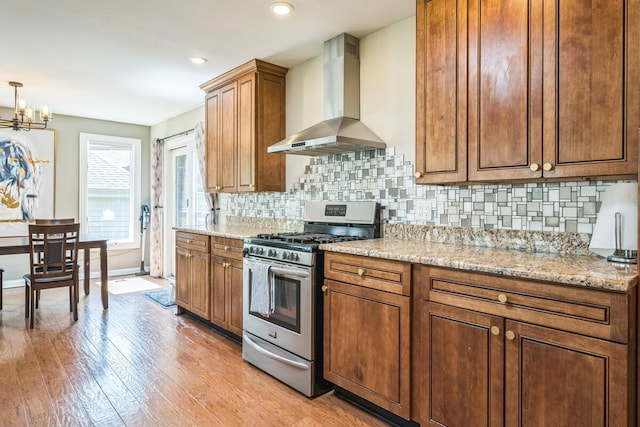 kitchen with backsplash, wall chimney exhaust hood, stainless steel gas range oven, and light wood-style floors