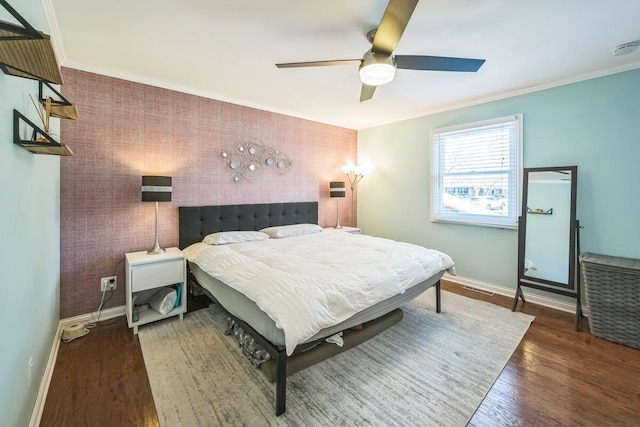 bedroom with baseboards, an accent wall, wood finished floors, ceiling fan, and crown molding