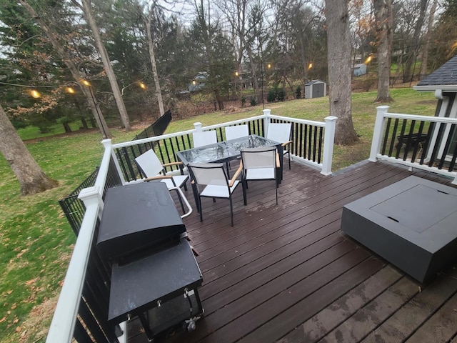 wooden deck featuring a lawn, outdoor dining area, an outdoor structure, grilling area, and a storage unit