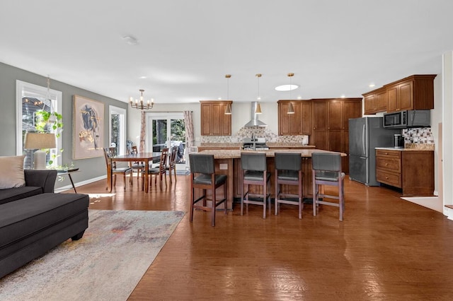 kitchen featuring wall chimney exhaust hood, decorative backsplash, freestanding refrigerator, and an inviting chandelier