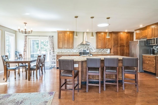 kitchen with wall chimney exhaust hood, brown cabinetry, backsplash, and appliances with stainless steel finishes