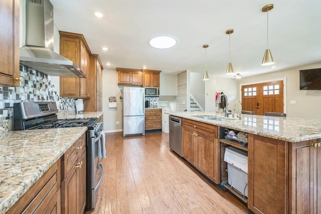 kitchen featuring wall chimney range hood, a sink, decorative backsplash, light wood-style flooring, and appliances with stainless steel finishes