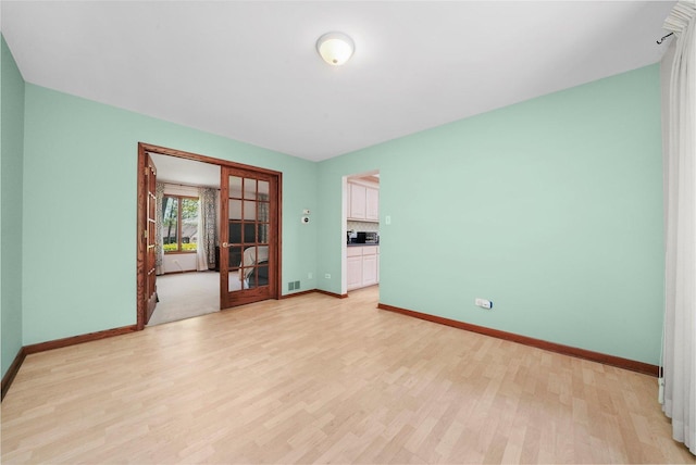 spare room with french doors, light wood-style floors, and baseboards