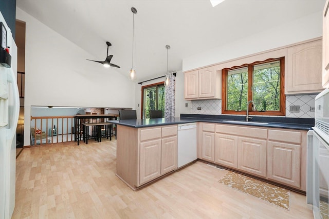 kitchen featuring a sink, white appliances, light brown cabinets, dark countertops, and lofted ceiling