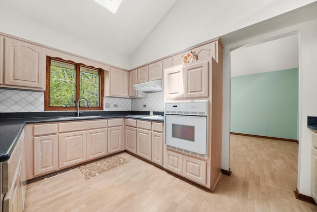 kitchen with oven, a sink, under cabinet range hood, light brown cabinetry, and lofted ceiling