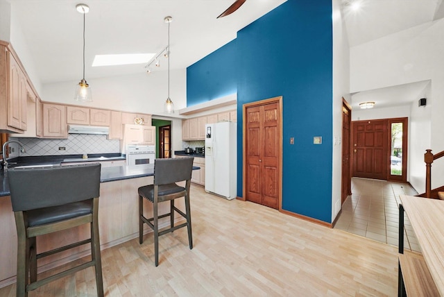 kitchen featuring white appliances, high vaulted ceiling, under cabinet range hood, a peninsula, and dark countertops