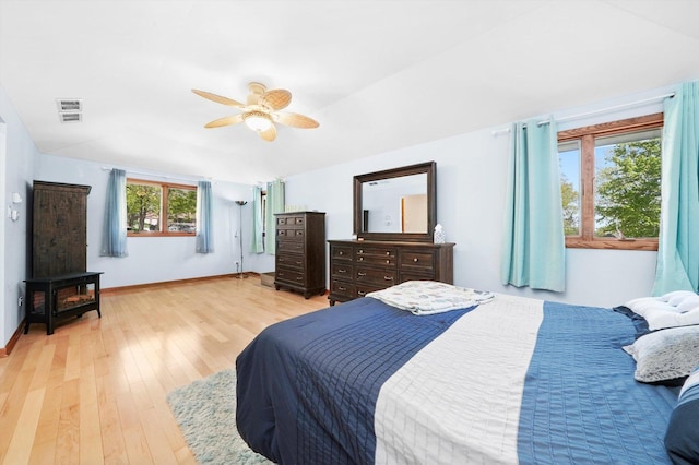 bedroom with a wood stove, light wood finished floors, baseboards, ceiling fan, and lofted ceiling
