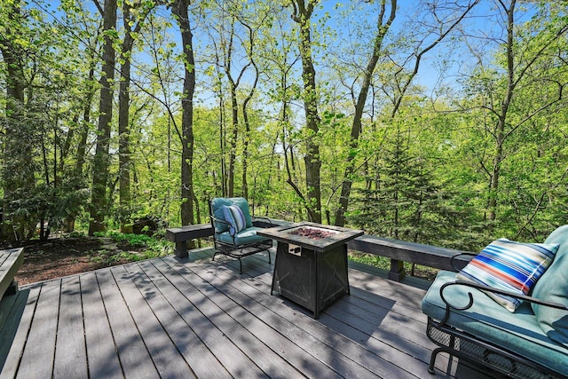 wooden deck featuring an outdoor fire pit and a wooded view