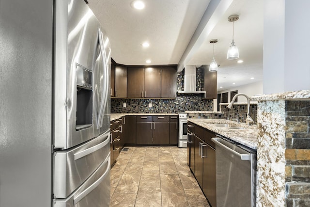 kitchen featuring wall chimney exhaust hood, a sink, dark brown cabinetry, decorative backsplash, and appliances with stainless steel finishes