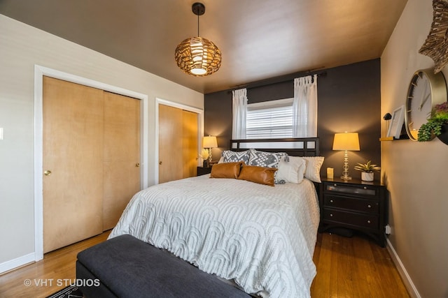 bedroom featuring baseboards, wood finished floors, and two closets