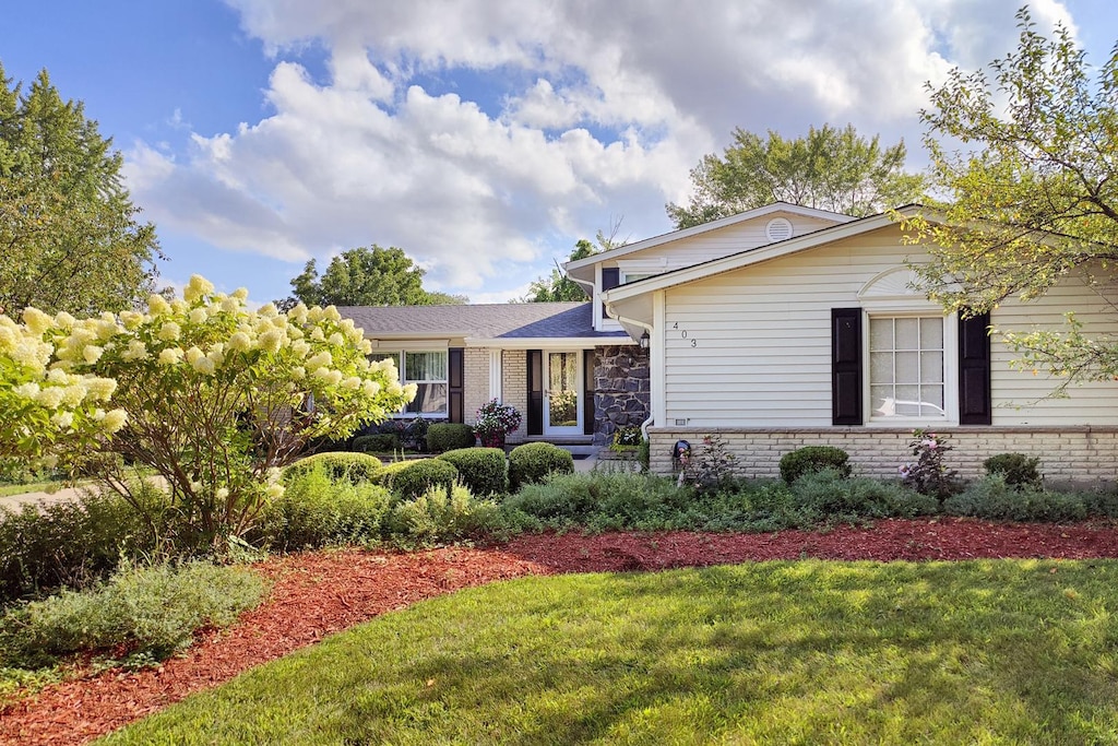 view of front of house featuring brick siding, a shingled roof, and a front yard