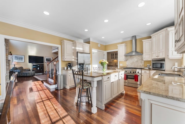 kitchen with wall chimney range hood, a center island, light stone countertops, stainless steel appliances, and a sink