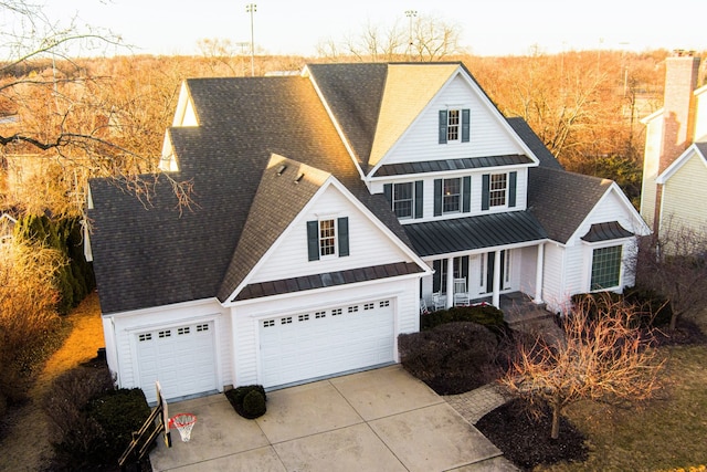 traditional-style house featuring a standing seam roof, a porch, metal roof, an attached garage, and driveway