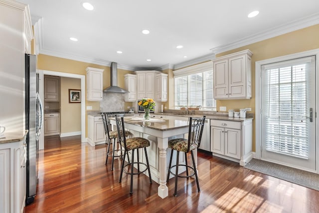 kitchen with crown molding, appliances with stainless steel finishes, wall chimney range hood, and a kitchen breakfast bar