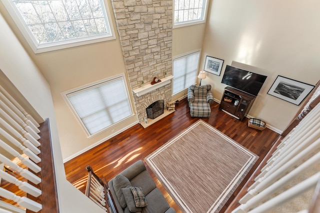 living room with a stone fireplace, a towering ceiling, wood finished floors, and baseboards