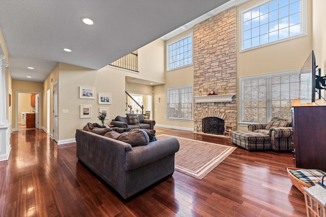 living room with a towering ceiling, a stone fireplace, wood finished floors, stairs, and baseboards