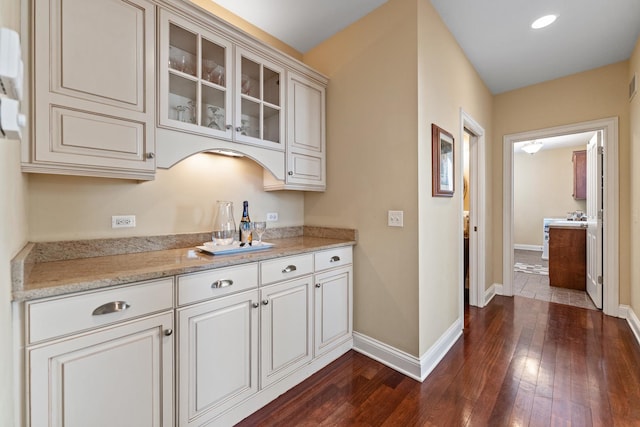 kitchen with glass insert cabinets, baseboards, light stone counters, and dark wood finished floors