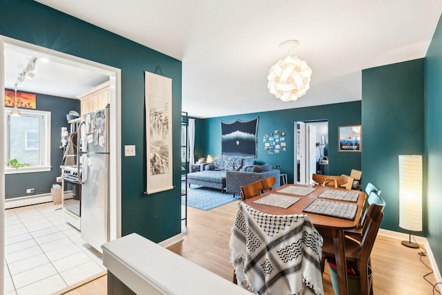 dining room featuring track lighting, a baseboard radiator, wood finished floors, and baseboards