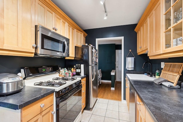 kitchen with light brown cabinets, light tile patterned floors, dark countertops, appliances with stainless steel finishes, and a sink