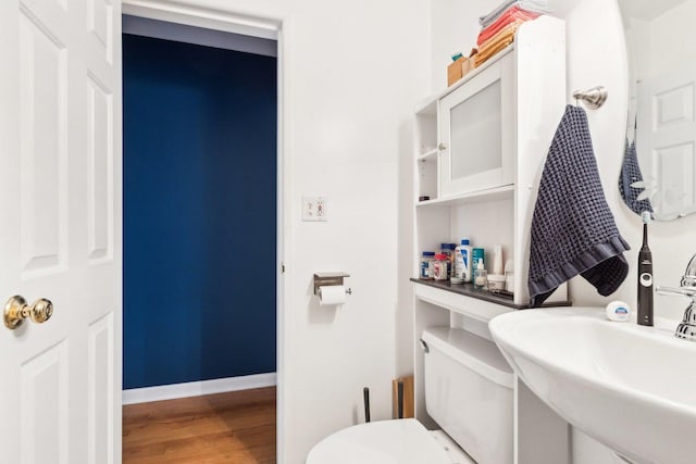 half bathroom featuring toilet, wood finished floors, a sink, and baseboards