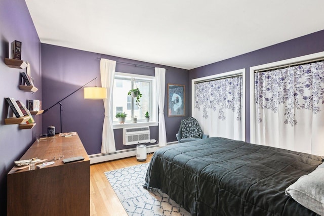 bedroom featuring light wood finished floors, baseboard heating, and a wall unit AC