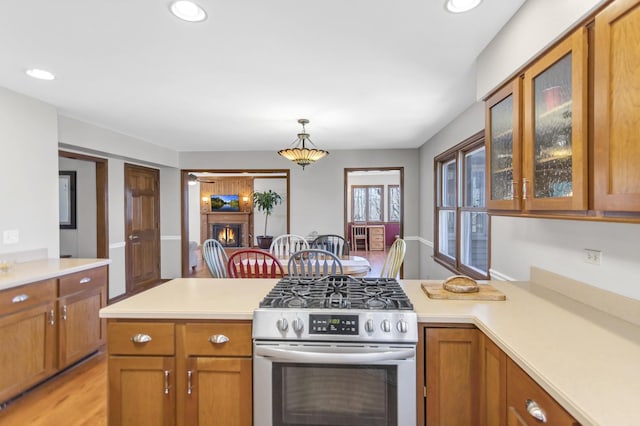 kitchen with brown cabinetry, a peninsula, gas stove, and light countertops
