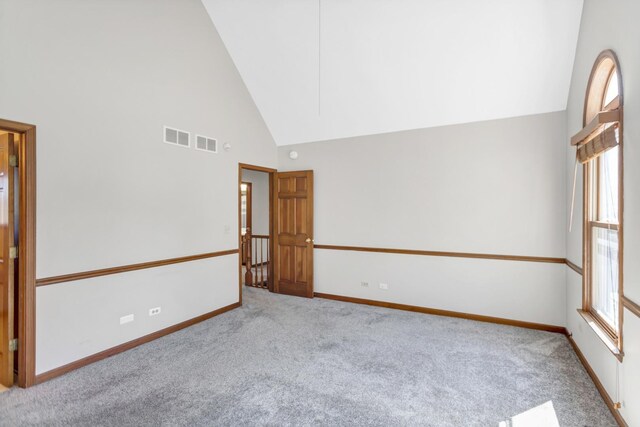 carpeted empty room with high vaulted ceiling, baseboards, and visible vents