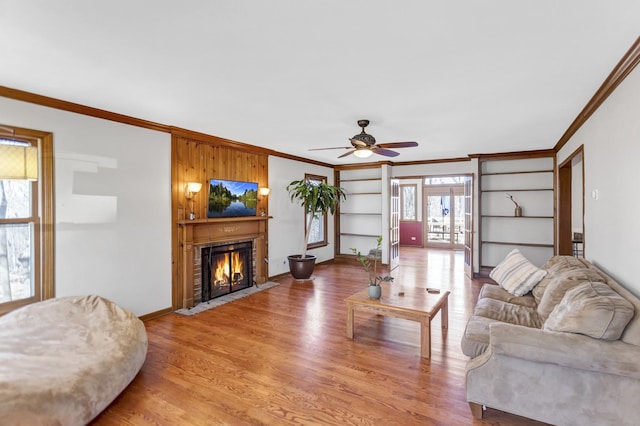 living room with baseboards, ornamental molding, a ceiling fan, light wood finished floors, and a fireplace with flush hearth