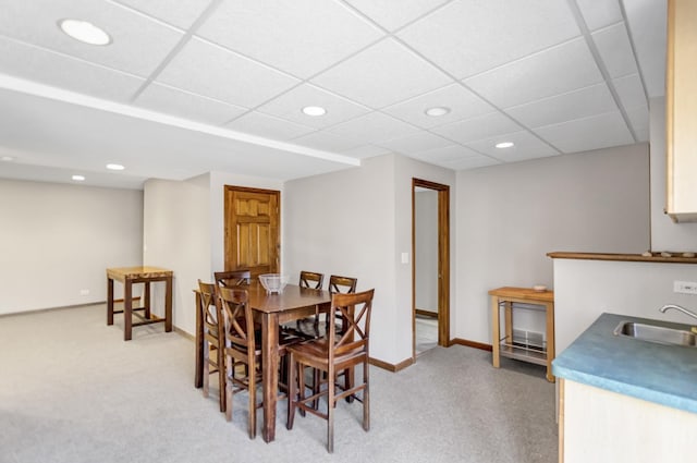 carpeted dining space with a sink, a drop ceiling, baseboards, and recessed lighting
