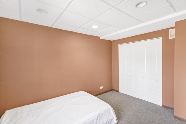 bedroom featuring visible vents, baseboards, a closet, carpet flooring, and a drop ceiling