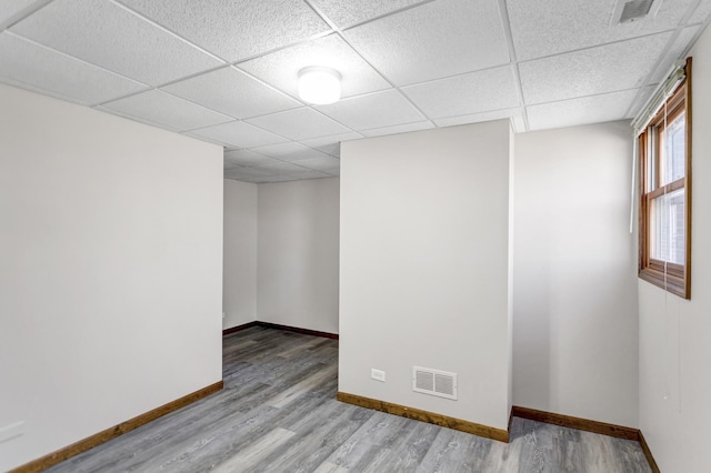 empty room featuring wood finished floors, baseboards, a drop ceiling, and visible vents