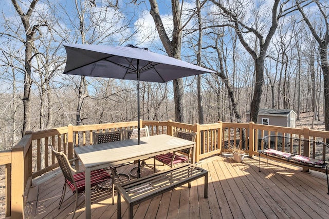 wooden deck with outdoor dining space, a shed, a view of trees, and an outbuilding