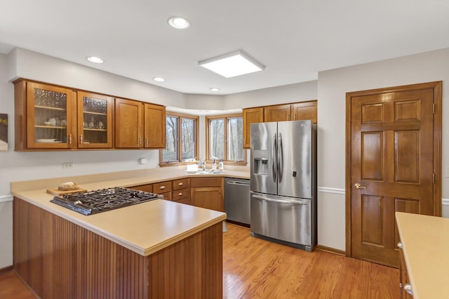 kitchen with a peninsula, light countertops, glass insert cabinets, and stainless steel appliances