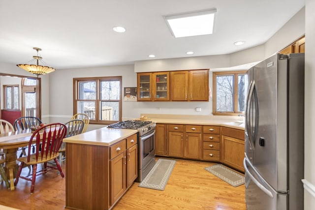 kitchen featuring a sink, appliances with stainless steel finishes, a peninsula, brown cabinets, and light wood finished floors