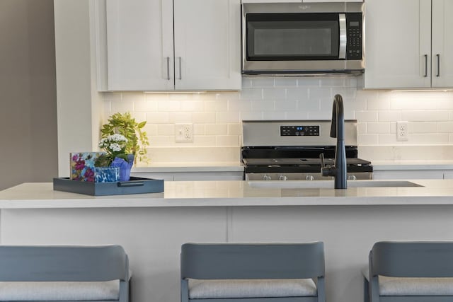 6367 Jasmine Ave, Portage, IN 46368 - kitchen with light countertops, a breakfast bar, backsplash, and appliances with stainless steel finishes
