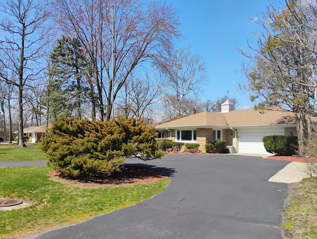 single story home featuring a garage, driveway, a chimney, and a front lawn