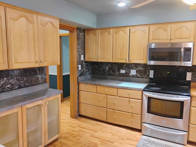 kitchen with light brown cabinets, glass insert cabinets, light wood-style flooring, backsplash, and stainless steel appliances
