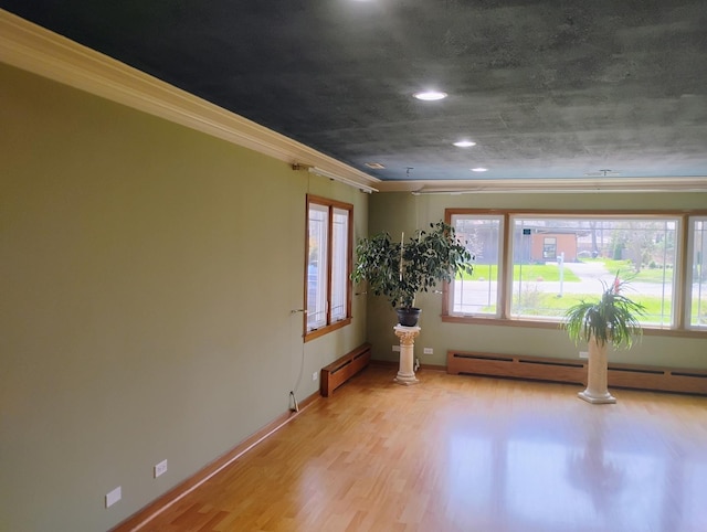 empty room featuring crown molding, baseboards, light wood finished floors, and baseboard heating