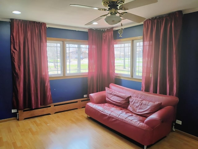 sitting room with wood finished floors, ceiling fan, plenty of natural light, and a baseboard heating unit
