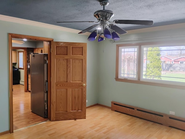 unfurnished bedroom with baseboards, freestanding refrigerator, a textured ceiling, light wood-style flooring, and a baseboard heating unit