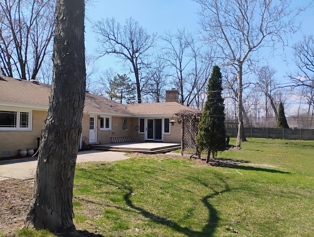 back of house with a wooden deck, a chimney, fence, and a lawn